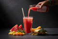 Summer Splash cold-pressed juice being poured into a glass with fresh watermelon, pineapple, cantaloupe, mint, and ginger